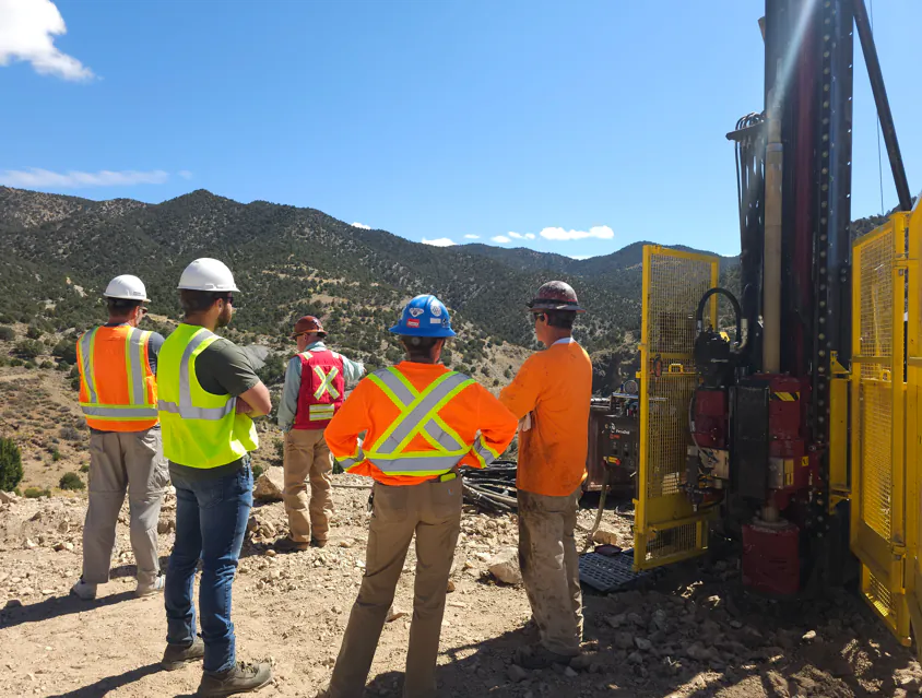 Burgex field engineers in hard hats and safety vests reviewing a core drilling rig in the mountains